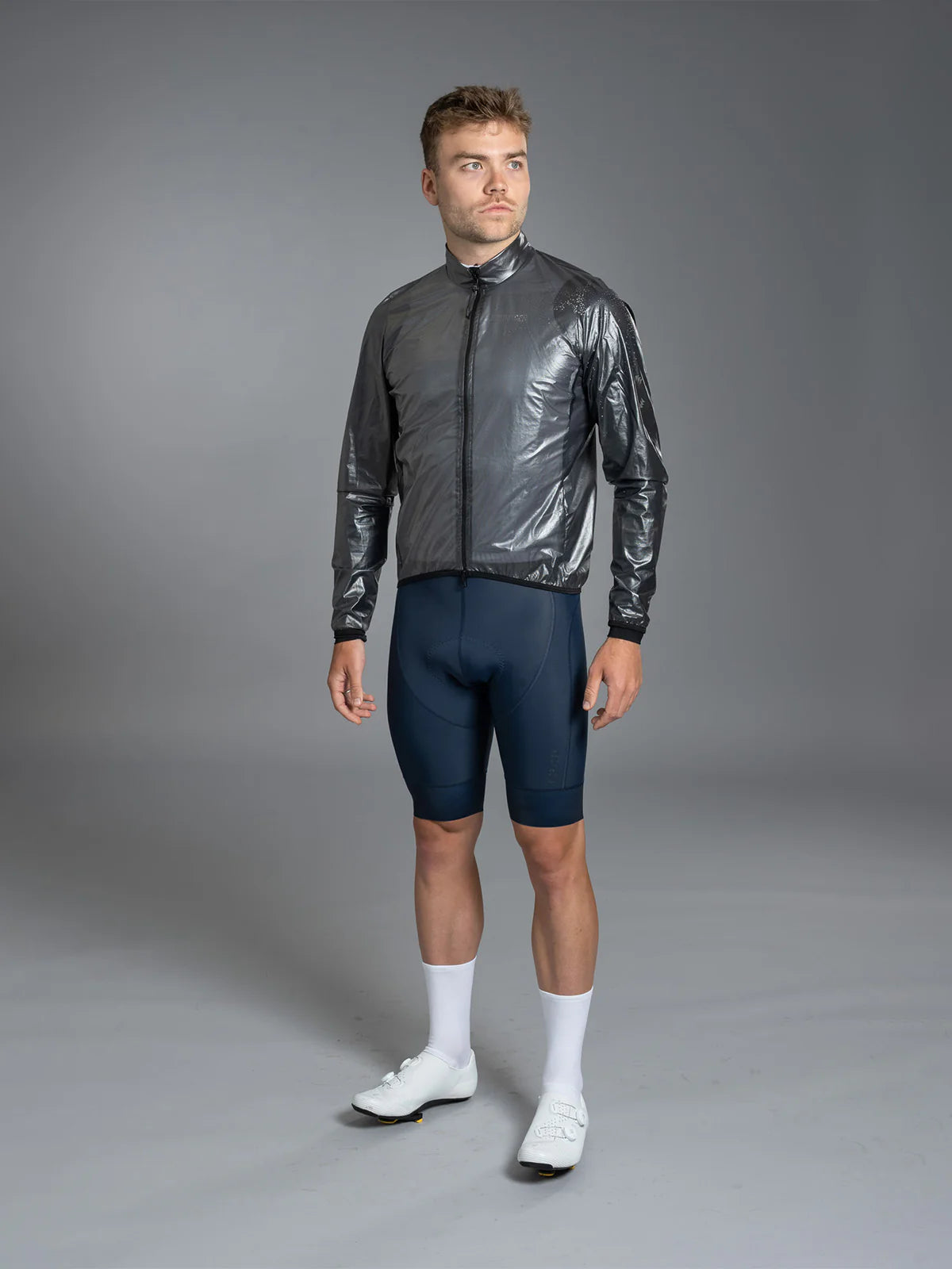 Man wearing a shiny black jacket and dark blue cycling shorts on a gray background