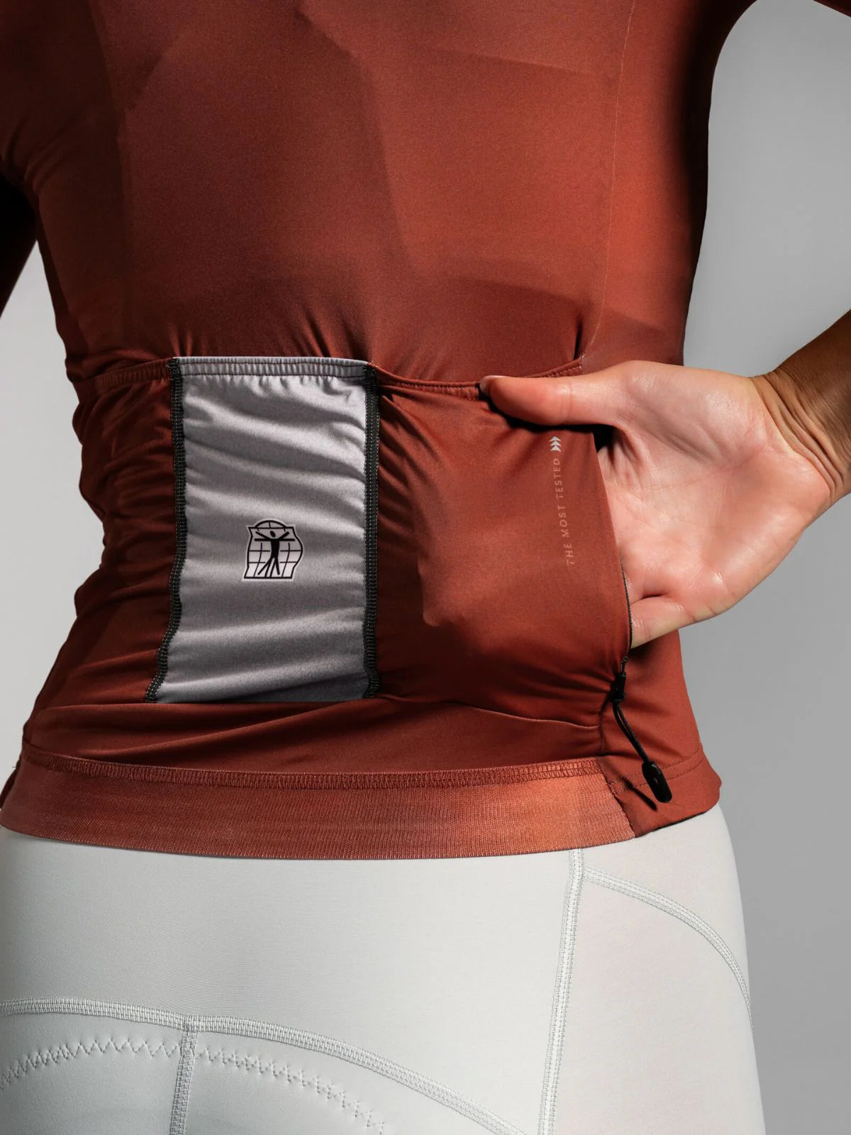 Close-up of a person wearing a brown athletic shirt with a gray pocket, on a gray background.