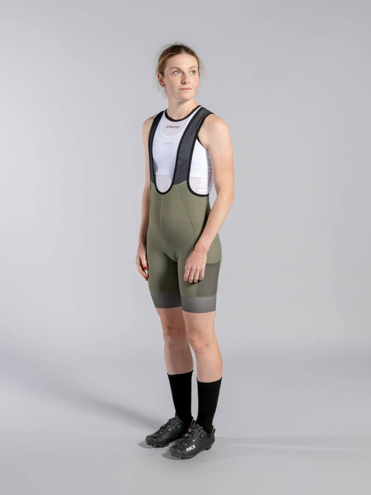 Person wearing a green cycling outfit with black bib shorts on a gray background
